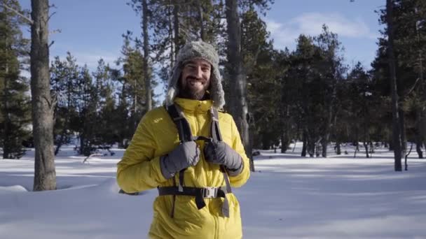 Retrato de um jovem caminhante olhando diretamente para a câmera perto de uma floresta montanhosa nevada. — Vídeo de Stock