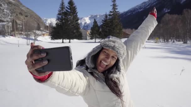 アフリカ系アメリカ人女性がセルフィーを撮るか、雪の山の中で携帯電話でビデオ通話をする. — ストック動画