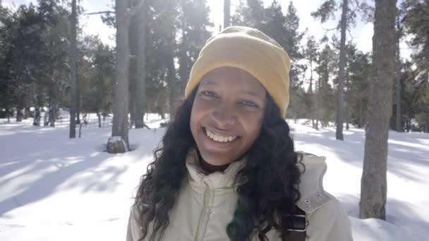 幸せなアフリカ系アメリカ人女性の肖像冬休みに雪の森の中に立っているカメラを見て. — ストック動画