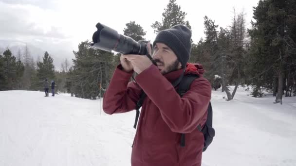 Fotógrafo profissional tirando uma foto na floresta de inverno nas montanhas. Um homem fotografando a paisagem natural — Vídeo de Stock