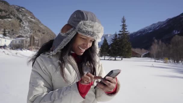 Mulher latina usando telefone na floresta de inverno com paisagem nevada. Menina alegre nas montanhas frias tipos de seu telefone celular. — Vídeo de Stock