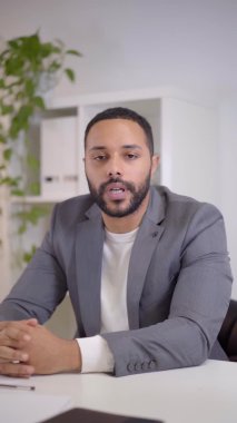 Dikey video. Ciddi bir kameraya bakan Latin bir iş adamının webcam görüntüsü. Kamerayla konuşurken sinirliyim..