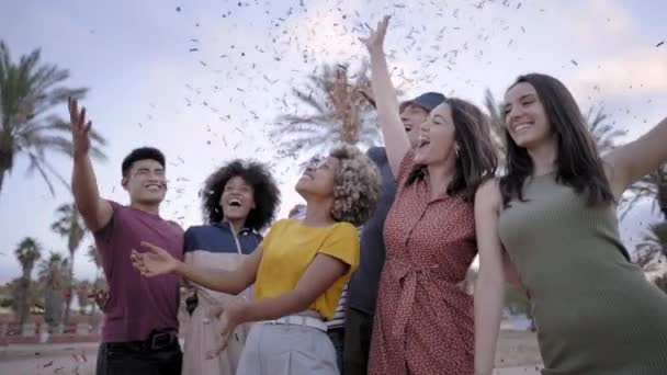 Mouvement lent d'un groupe multiethnique de jeunes qui s'amusent avec des confettis à l'extérieur. Concept de célébration, fête, plaisir, joie. — Video