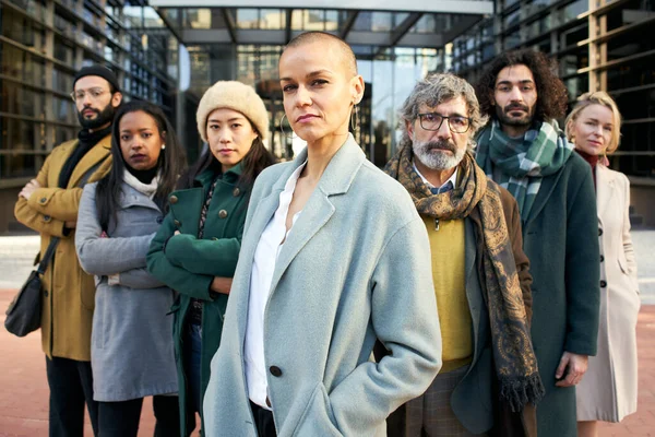 A group of serious business people from a company led by an empowered shaved air woman. Looking at camera portrait of a group of co-workers of diverse races and ages. — Stock Photo, Image
