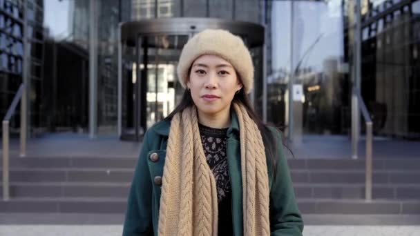 หญิงสาวชาวเอเชียที่จริงจังมองกล้อง ผู้หญิงจีนอยู่ข้างนอก ใกล้กับตึกบริษัทในเมือง — วีดีโอสต็อก