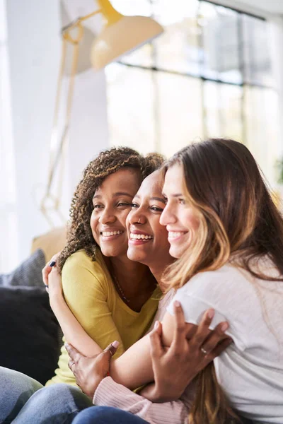 Foto vertical de tres amigas felices abrazándose sonriente.Mujeres divertidas juntas celebrando sentadas en el sofá de la sala de estar — Foto de Stock