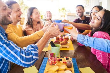Çok kültürlü insanlar kahvaltlarını yapıp, kahkaha atıyorlar. Teras barında mutlu topluluk eğlencesi. Komik bir arkadaş grubu gülüyor ve meyve suyu içiyor..