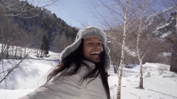 En vacker afrikansk kvinna njuter av en vintermiljö i den snöiga fjällskogen. Glada titta på kameran av leende flicka. — Stockvideo