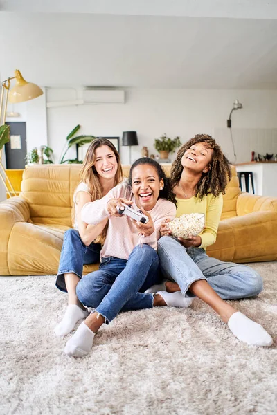 Вертикальне фото Група молодих жінок багаторасових молодих друзів грають у відеоігри разом вдома. Тільки жінки грають і їдять попкорни . — стокове фото