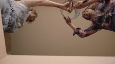 İki neşeli beyaz kızın ev eşyaları paketlediği karton bir kutunun içinden bak. İki gülümseyen kızın karton kutuyu açtığı yakın plan..