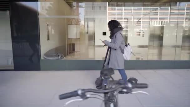 Boční pohled Business Woman walking pomocí chytrého telefonu městské ulice s e-scooter. Mladí lidé jezdit ekologické dopravy zdravý životní styl s moderním architektonickým zázemím. — Stock video