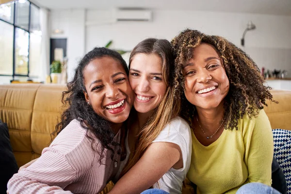 3人の混合レース幸せな女性の友人は笑顔を抱きます-面白い女性が一緒にカメラの自撮りを見てリビングルームのソファに座って祝う. — ストック写真