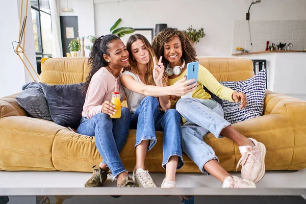 3人の幸せな女性の友人が笑顔で自撮りし、自宅で楽しんでいます-一緒にリビングルームのソファに座って祝う携帯電話を使用して面白い女性 — ストック写真