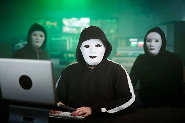 Masked Hacker is Using Computer for Organizing Massive Data Breach Attack on Corporate Servers. Theyre in Underground Secret Location Surrounded by Displays — Foto de Stock