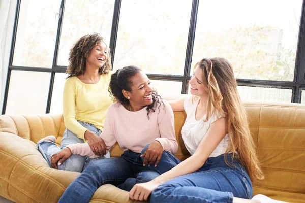 3人の若いです多人種間の女の子話しています座っていますソファリビングルームホーム. — ストック写真