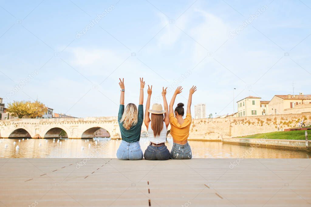Rear view of happy young women friends sitting on the lake