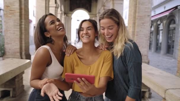 Drie vrolijke vrouwen die buiten mobiel bellen. Groep lachende vrouwelijke vrienden kijken naar sociale media op de smartphone — Stockvideo