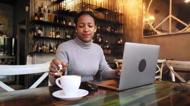 African American Business woman working with laptop at cafe bar restaurant. Female remote worker using computer sitting in a table and drinking coffee indoors — ストック動画