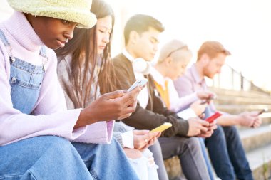 Bir grup çok ırklı arkadaş dışarıda cep telefonu kullanıyor ve ciddi yüzlü akıllı telefonları izliyorlar. Çeşitlilik İnsanlarla Tanışıyor Rahatlatıcı Bağlantı İletişim Toplumu Kavramı. 
