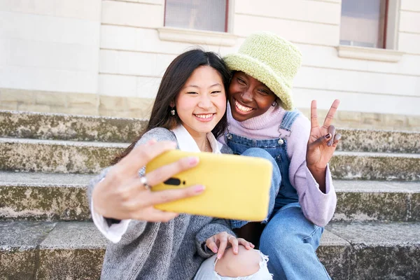 Smiling selfie of Two cheerful female friends having fun. Interracial Couple taking picture with smart mobile phone. Happy people enjoying vacations only for girls — Stock Fotó
