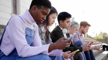 Bir grup çok ırklı arkadaş dışarıda cep telefonu kullanıyor ve ciddi yüzlü akıllı telefonları izliyorlar. Çeşitlilik İnsanlarla Tanışıyor Rahatlatıcı Bağlantı İletişim Toplumu Kavramı. 