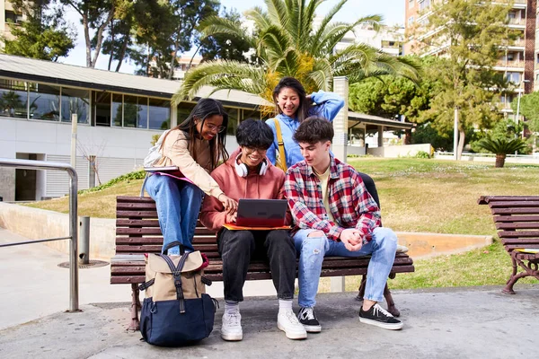 Young international college students reading books, studying on laptop, preparing for exam or working on group project while sitting on bench of college campus university — Stock Fotó