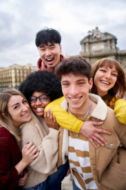 Vertical Smiling selfie of a group of happy friends outdoors in the city. Young tourists take pictures of their vacation with a smart phone. People having fun on a student trip in Europe.