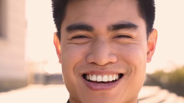 Dışarıdan gülümseyen bir Çinli 'nin, kameraya bakıp gülen bir yüz ve dostane bir bakışla dış görünüşü. Neşeli Asyalı genç bir adamın mutlu insan yüzüne yakın çekim. İnsanlar ve duygular. — Stok video