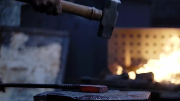 Estilo cinematográfico de um ferreiro em câmera lenta forjando um ferro quente na forja. Artesanato em obras antigas com fogo no fundo. — Vídeo de Stock