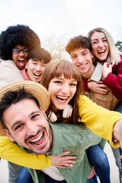 Vertical photo of Cheerful group of happy friends taking smiling selfie in piggyback. Three couple having fun together outdoors at park in the city. People enjoying travel in vacation holidays. — Foto de Stock