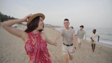 Kumsalda eğlenen mutlu bir grup genç. Neşeli arkadaşlar yaz günbatımının tadını çıkararak el ele koşarlar. Boş zaman ve topluluk kavramı. Yüksek kalite 4k görüntü