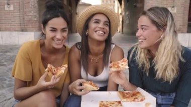 Şehrin merdivenlerinde oturan üç güzel kadın sokak tezgahından pizza yiyorlar. Mutlu kızlar hafta sonunun tadını çıkarıyorlar. Yüksek kalite fotoğraf