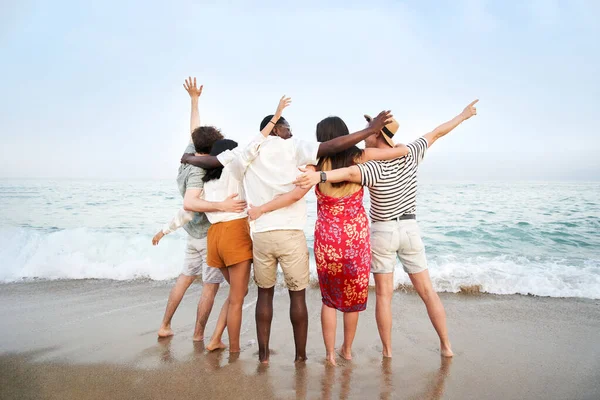 A group of friends with their backs to the camera enjoying the sea together - Multicultural multinational happy people hugging into the sun carefree and happiness, vacation on sea. High quality photo