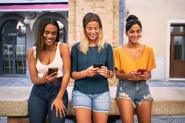 Dışarıda cep telefonu kullanan üç mutlu kadın. Bir grup gülümseyen bayan arkadaş akıllı telefondan sosyal medyayı izliyor. Yüksek kalite fotoğraf
