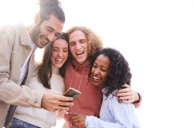 Isolated copy space white background. Four cheerful friends watching smartphone outdoors. People using digital device and sharing in social media togethers. High quality photo