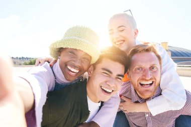 Sırt sırta verip gülen selfie çeken arkadaşlar güneşli bir günde birlikte eğlenen bir grup gencin kendi portresini çekiyorlar. Fotoğraf için kameraya bakan kızlar ve erkekler yüksek kaliteli pozlar.