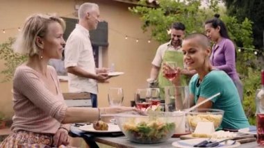 Bir grup mutlu arkadaş barbekü piknik partisinde kırmızı şarap içerek eğleniyorlar. Orta yaşlı insanlar arka bahçede lezzetli bir yemek yiyorlar. Yüksek kalite fotoğraf