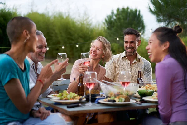 Happy middle-aged men and women toasting healthy food at farm house picnic - Life style concept with cheerful friends having fun together on afternoon relax time. High quality photo
