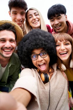 Gülümseyen selfie çeken neşeli bir arkadaş grubunun dikey fotoğrafı. Bir grup genç birlikte parkta eğleniyor tatillerde seyahatin tadını çıkarıyorlar. Yüksek kalite fotoğraf