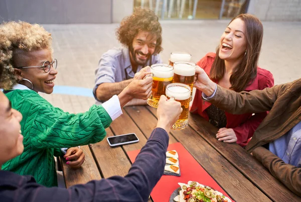 Group of happy friends toasting with beer while having lunch outdoors. The focus is on beers. High quality photo