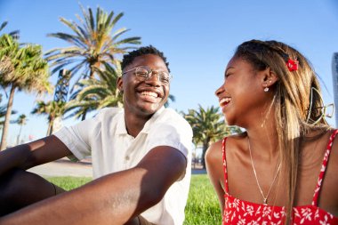 Neşeli genç Afrikalı çift parktaki ilk buluşmalarında gülüyor ve eğleniyorlar. Açık havada romantik aşıklar sahnesinde, çimenlerde oturup konuşuyorlar. Yüksek kalite fotoğraf