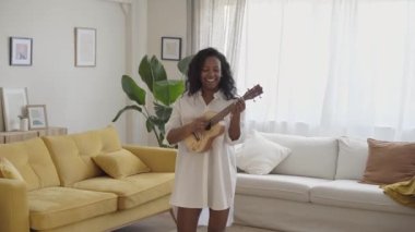 Young woman singer playing musical instrument sitting on the sofa at home. High quality photo