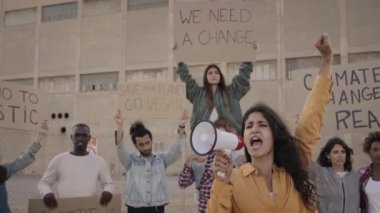 Slow motion of a Woman with a megaphone leading a protest, crowd of activists. People holding banners of fighting climate change is real. High quality FullHD footage