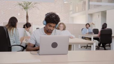 Employees celebrate listening music with headphones, have fun dancing at office. His colleagues work in the background. Managers enjoy success and victory. High quality 4k footage