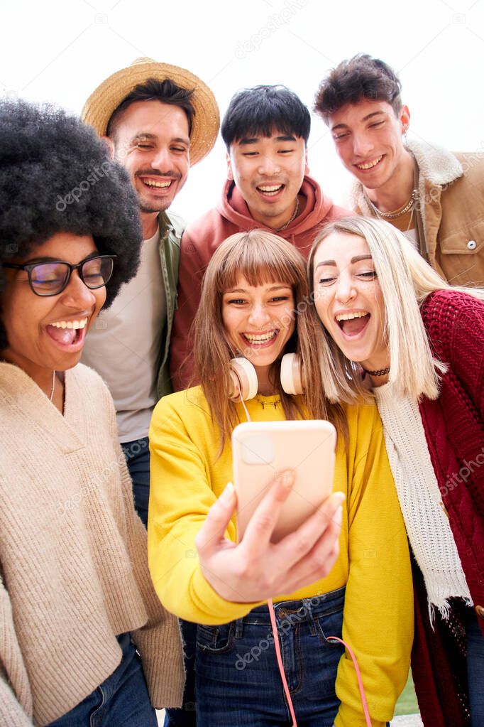 Vertical photo. Multicultural group of friends using cell phones and laughing. Cheerful students lined up and looking at smartphone screen Young people smiling and looking at their mobile High quality