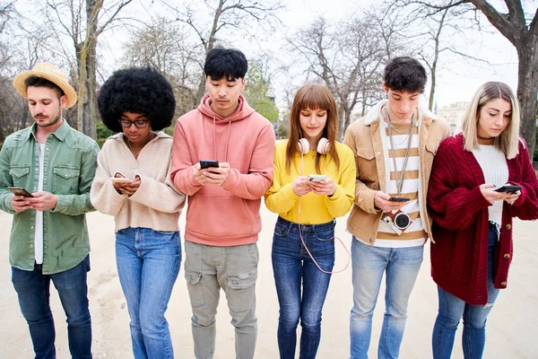 Group of young multiracial friends using smartphone ignoring each other. People and technology addiction in todays lifestyle. High quality photo