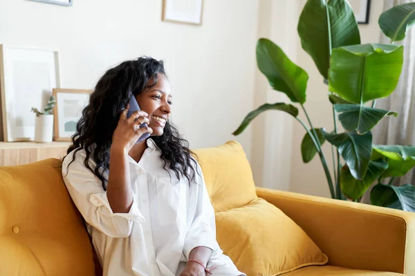 Cheerful Woman on a call mobile phone at home. Smiling lady is laying on the sofa. High quality photo