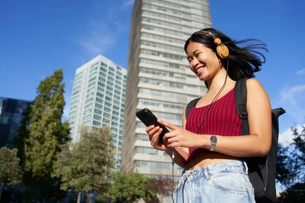 Happy asian people listens music with headphones on smartphone. City summer lifestyle. Smiling woman. High quality photo