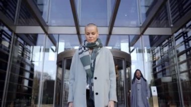 Successful young beautiful shaved head woman walking out business buildings and smiling. Attractive business female self-confident. Career empowered people. Crowed financial corporate center. High