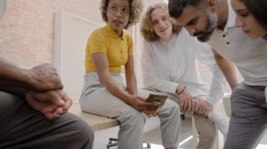 Business people watching cellphone and presenting project to multiethnic colleagues during casual business team meeting in office. High quality 4k footage
